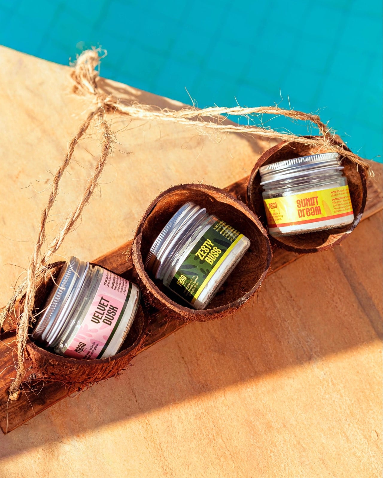 Manna Oils Zesty Bliss, Sunlit Dream and Velvet Dusk body butters arranged in coconut shells by the water