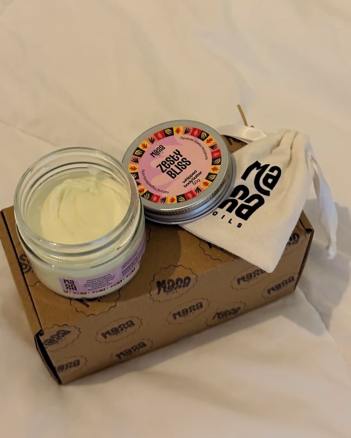 Open Manna Zesty Bliss body butter jar beside its delivery pouch
